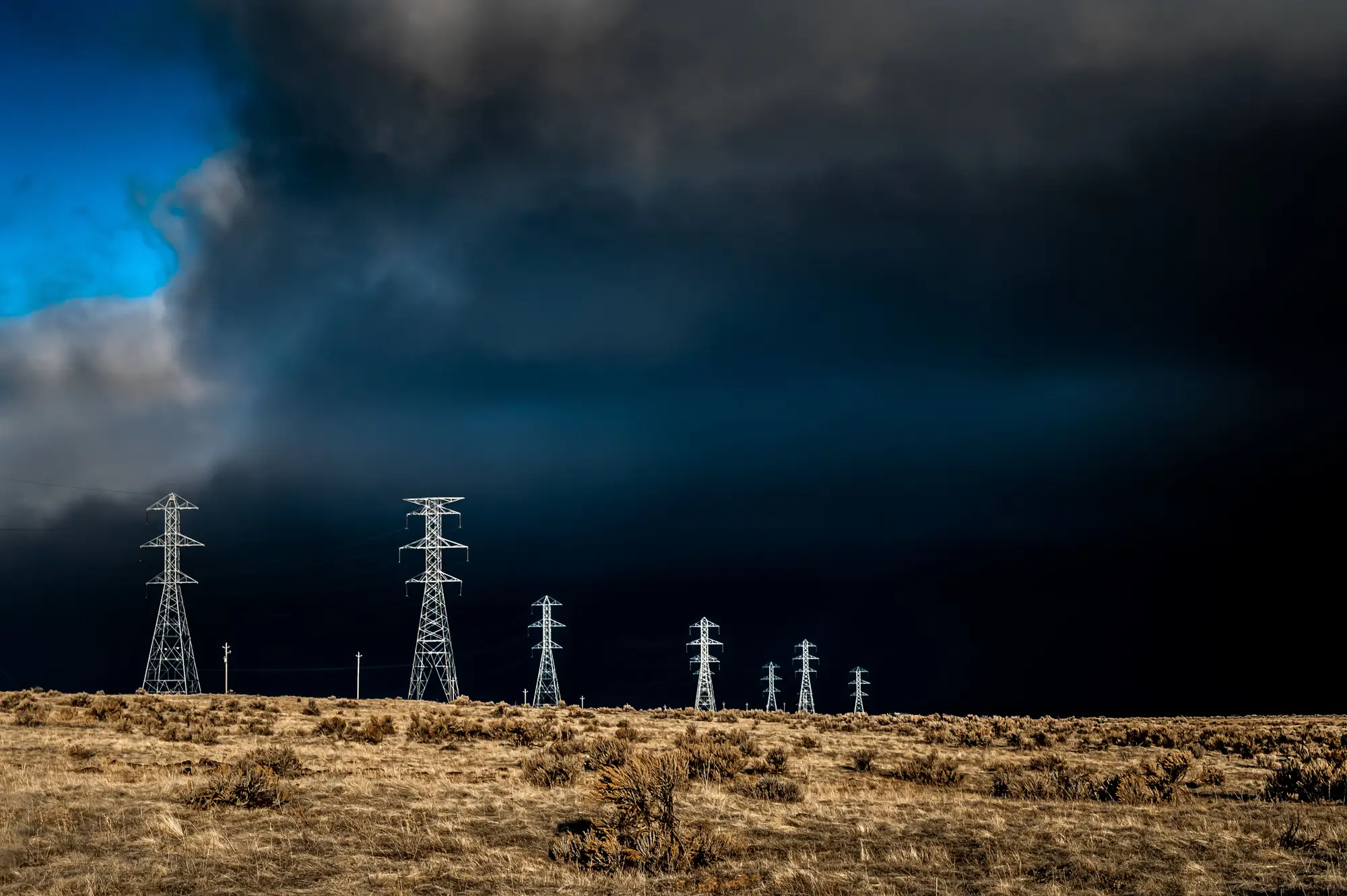 A squall line of black cloud moving over a row of transmission towers on open rangeland